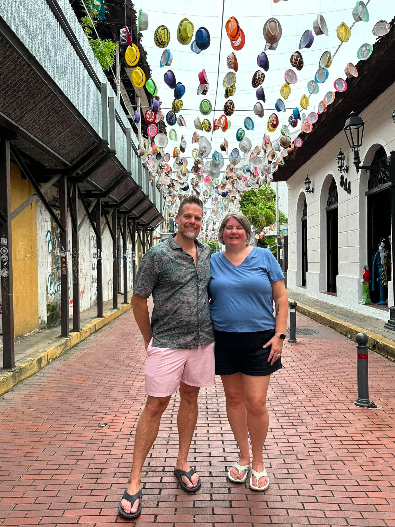 Heather and her husband under colorful hanging hats